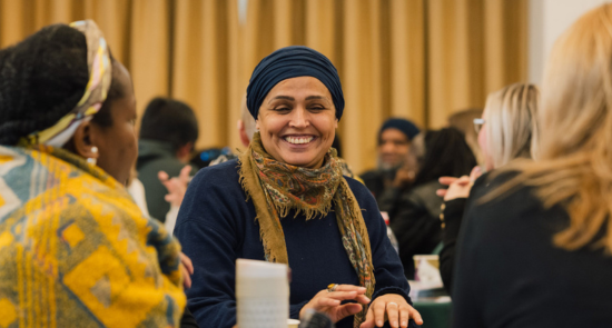 A woman smiling and talking to other people sat around a table)