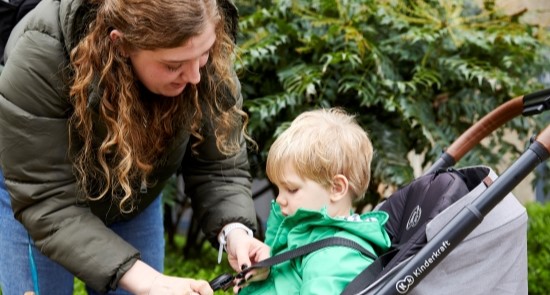 A woman strapping a child into a pushchair.)