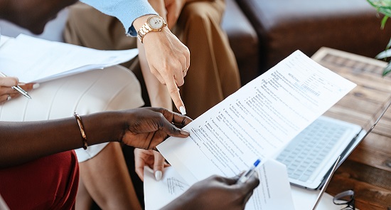 close up of different hands pointing at a document)