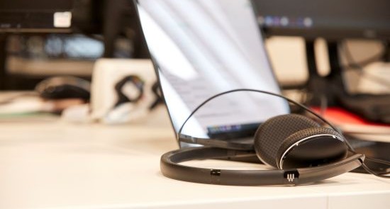 A pair of headphones on a desk in front of a laptop.)