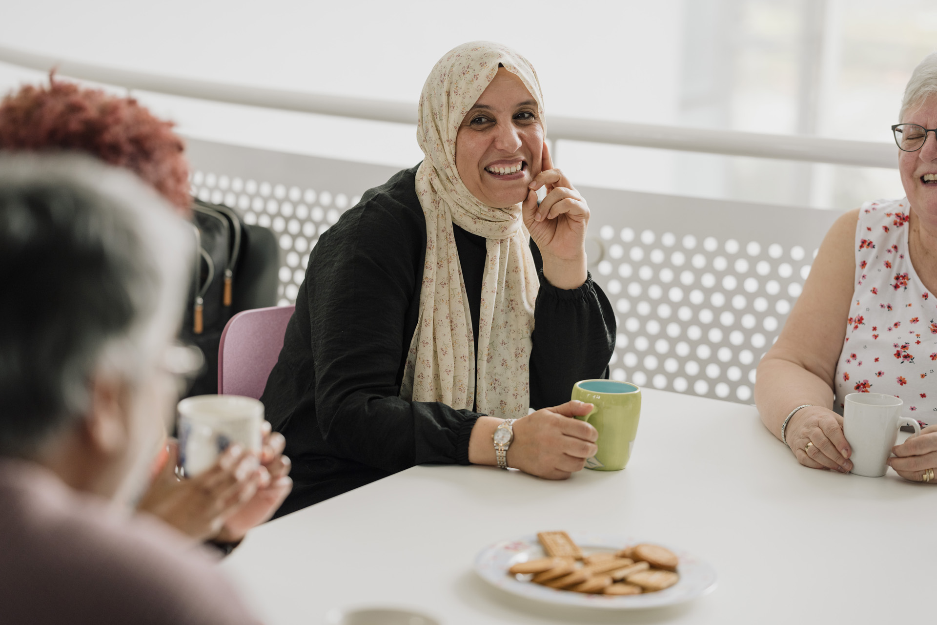 women sit around a table sharing tea and biscuits