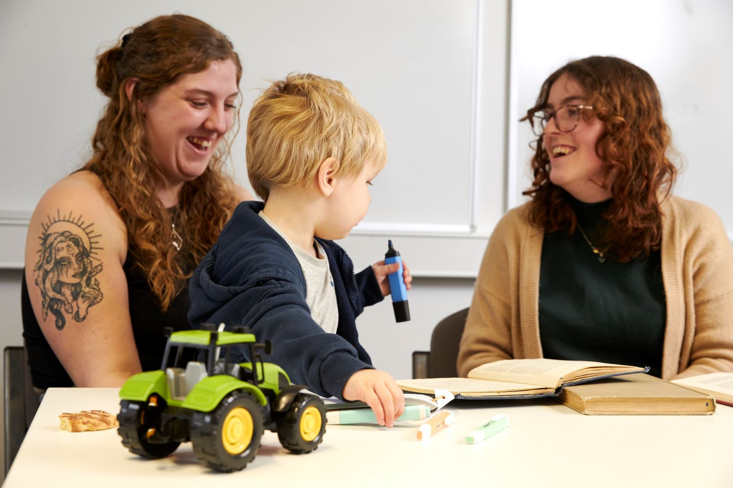 A toddler plays with toys whilst two women laugh