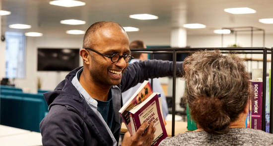 A person holding a book, smiling at another person)