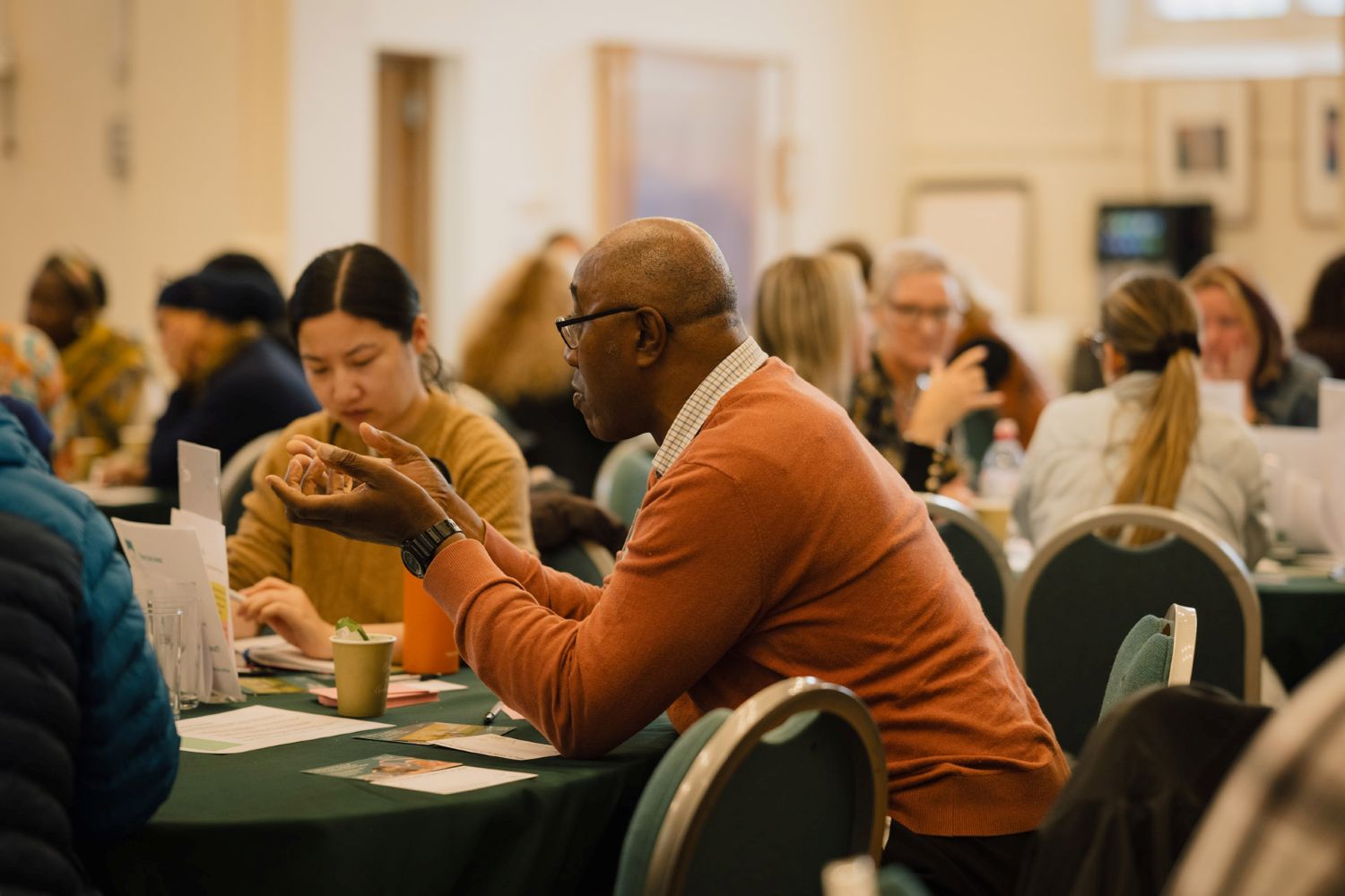 A man talking with other people, sat around a table